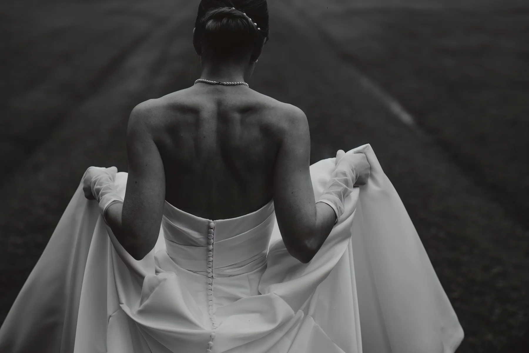 Sposa ripresa di spalle in bianco e nero mentre sistema l'abito